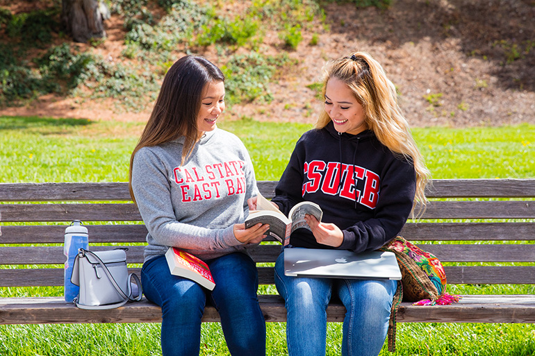 Two female students sitting on a bench and reading