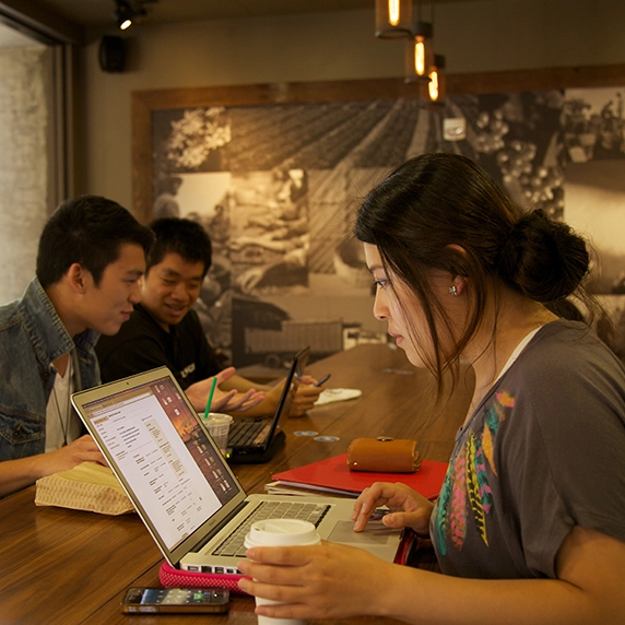 A student inside the campus café looking focused on their laptop.