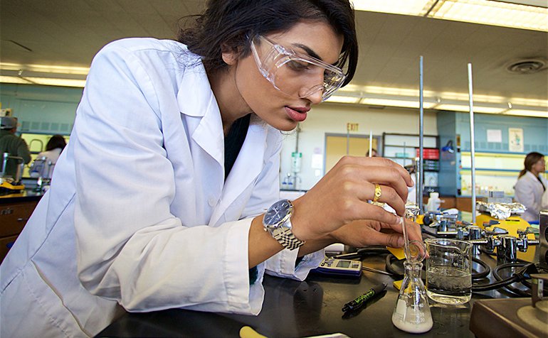 A chemistry student adds liquid to a beaker.