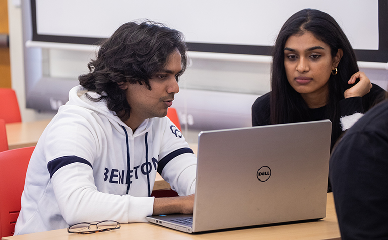 Two students working at laptop