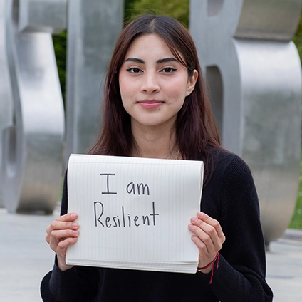Alumna Litzy Serrano a sign that says "I am resilient"