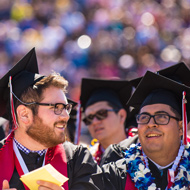 Three males smile in their cap and gown apparel at graduation