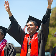 A student raises is hands in celebration at graduation