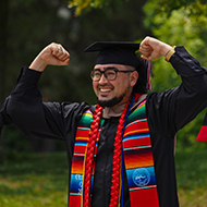 A student raises his arms in celebration at graduation