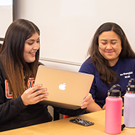 A young woman shows another her computer. 