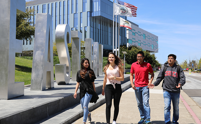 Four students walk by large East Bay letters
