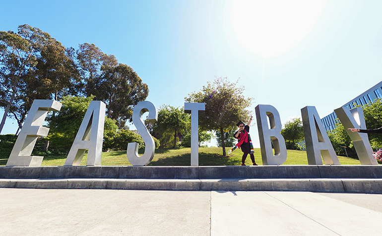 Student celebrating in front of East Bay letters