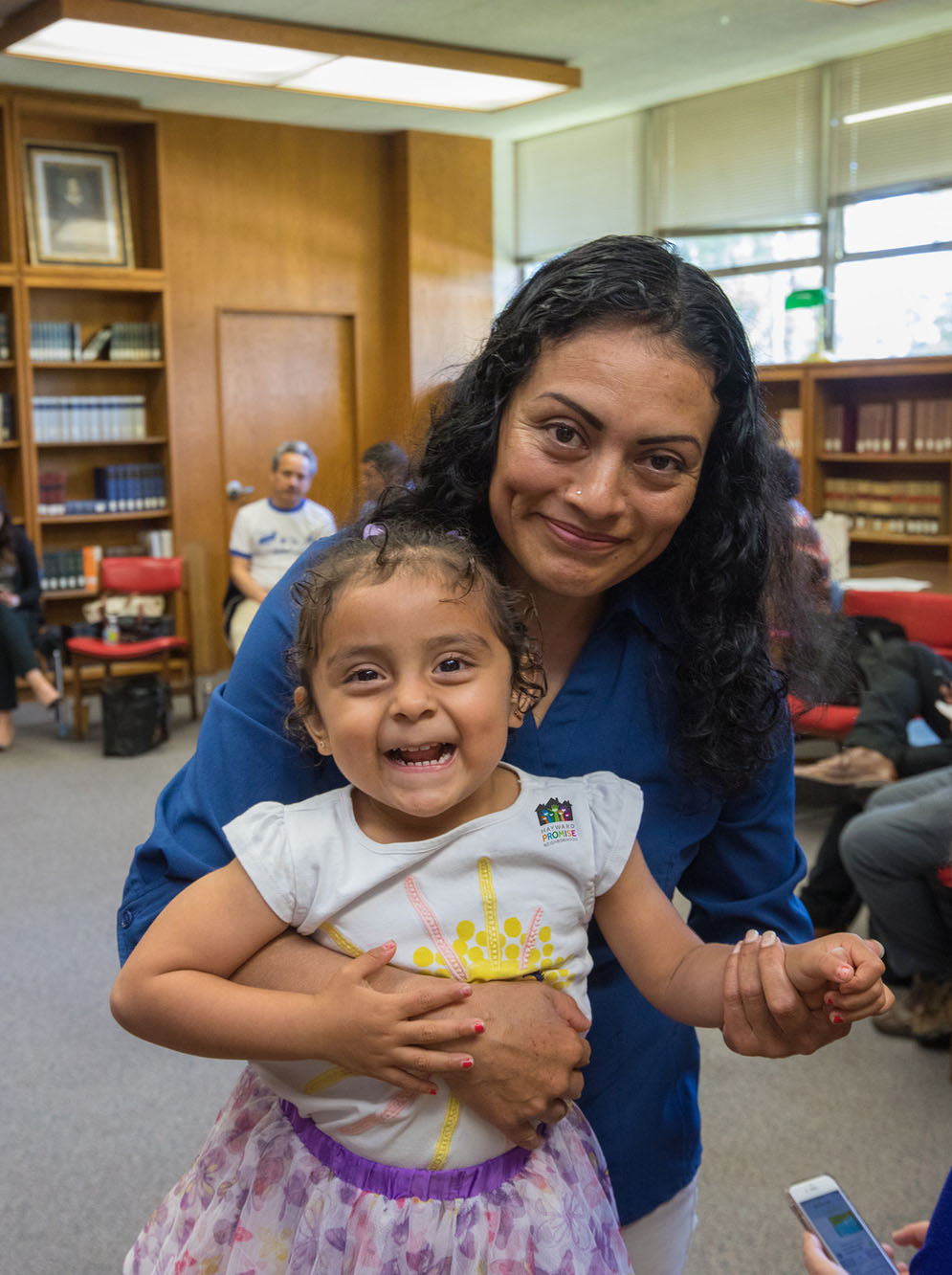 Woman holds young daughter with others seated in a circled behind them.