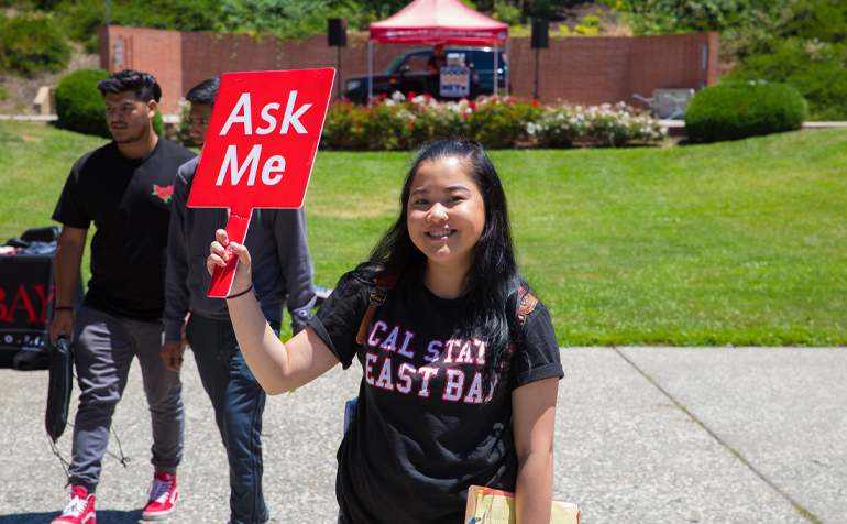 Student holding a sign that reads "Ask Me"