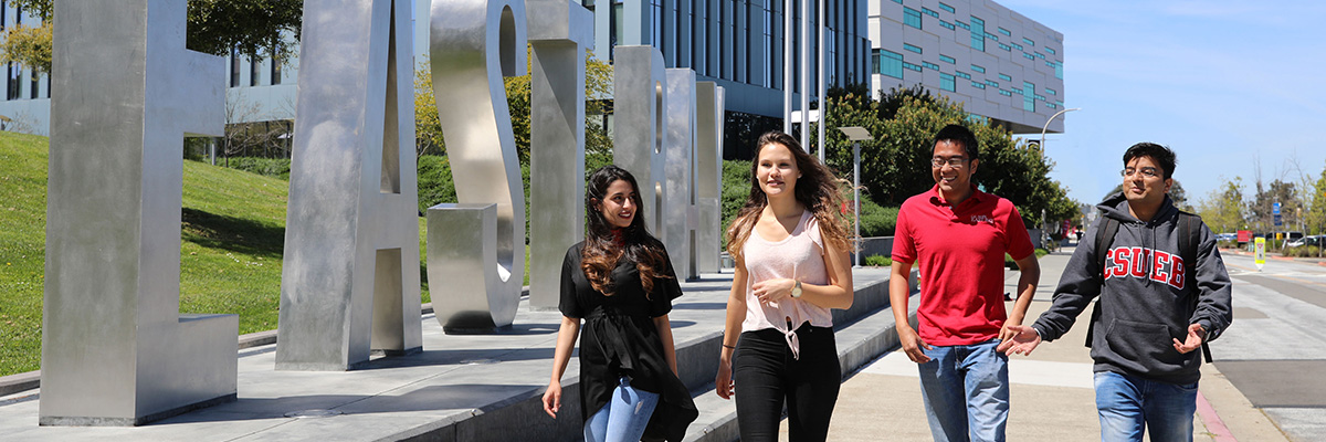 Group of four students walking side by side next to the East Bay letters monument