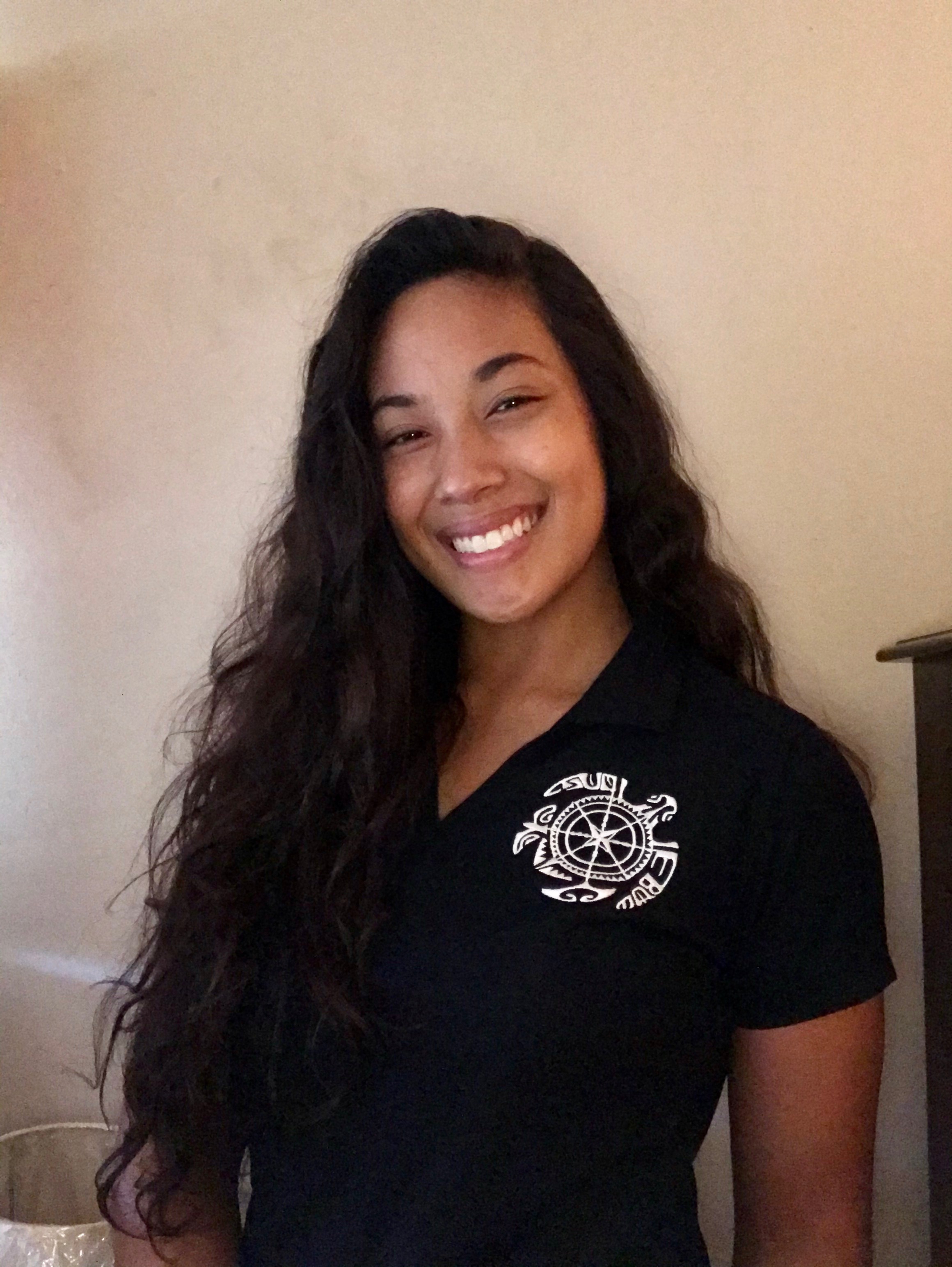 Woman with long, wavy hair smiling, standing in front of white wall