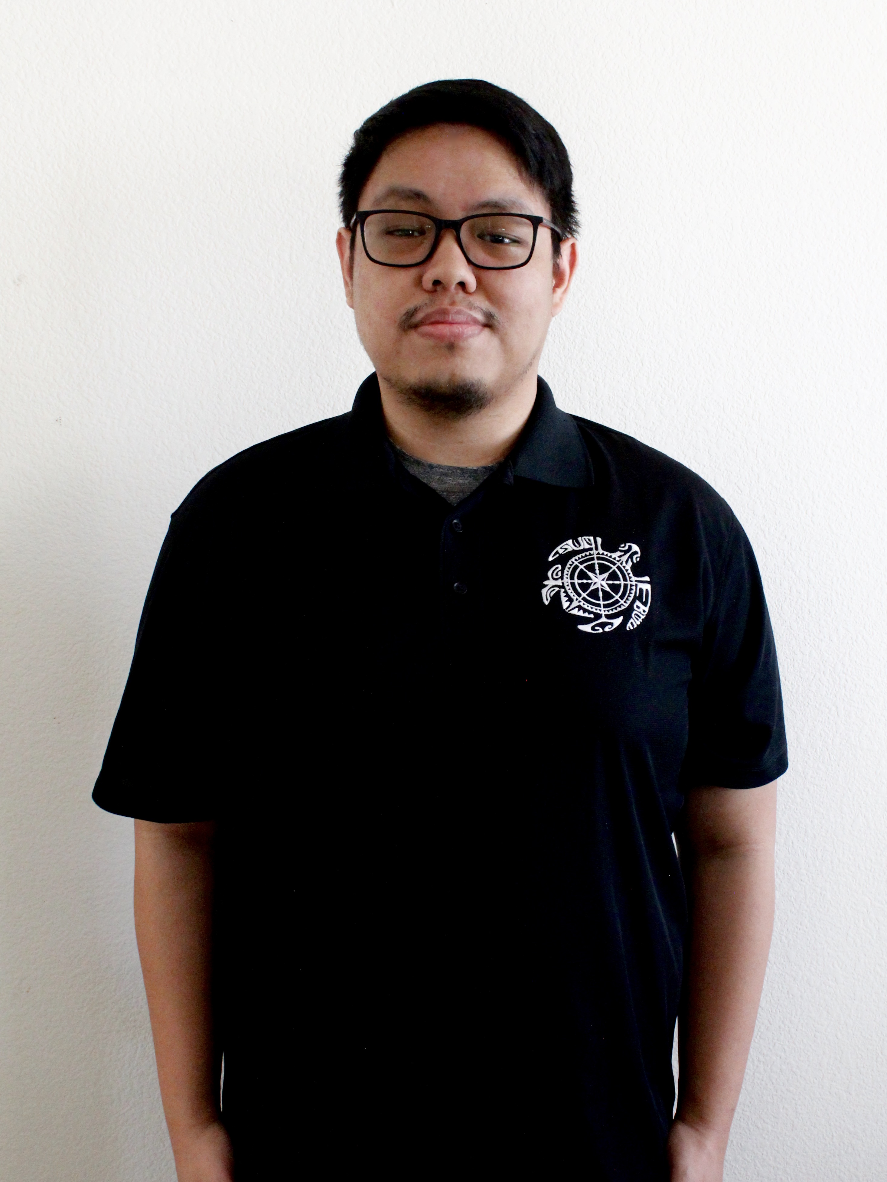 Man with black hair smiling, standing in front of white wall