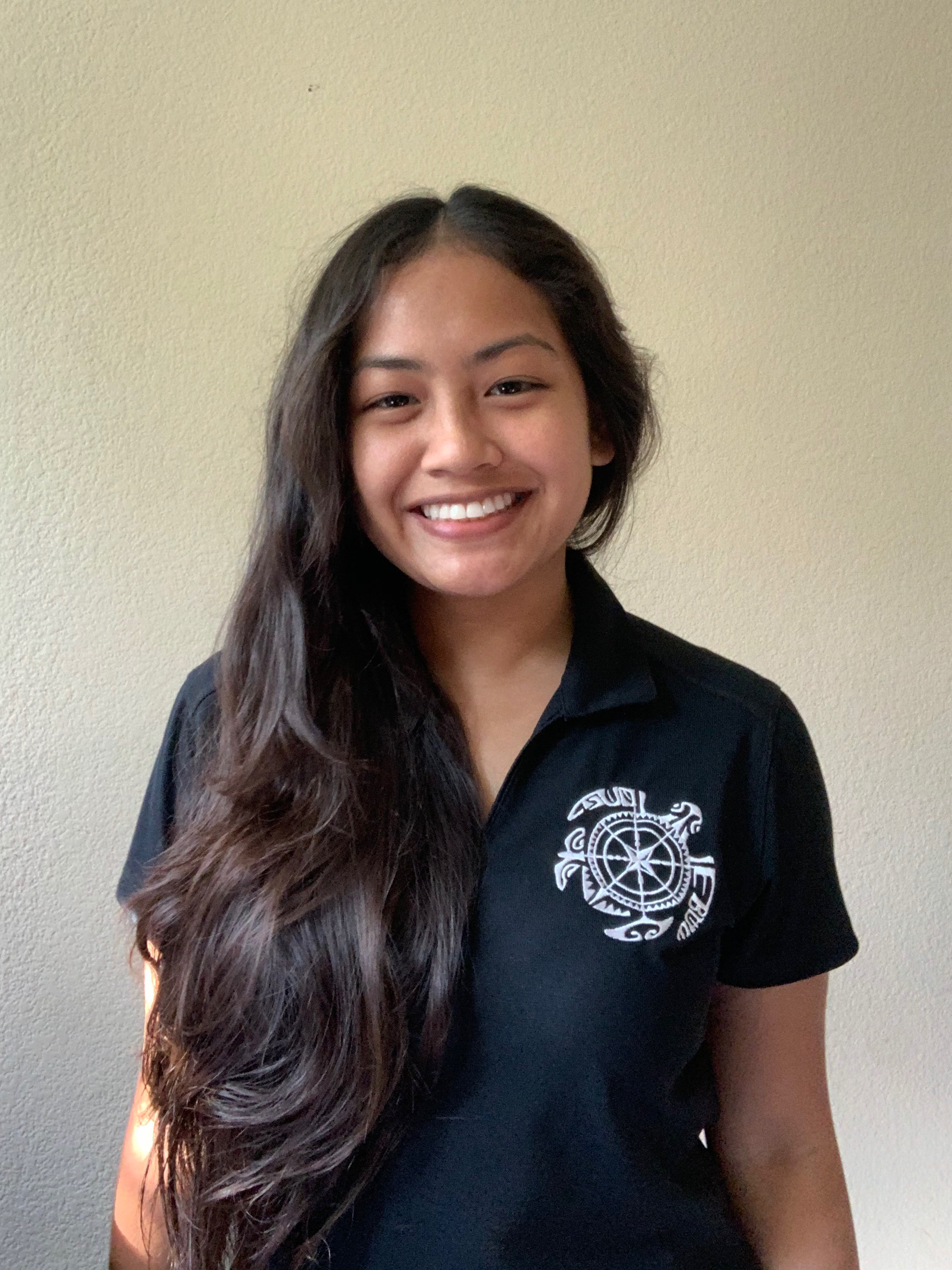 Woman with straight hair smiling, standing in front of white wall