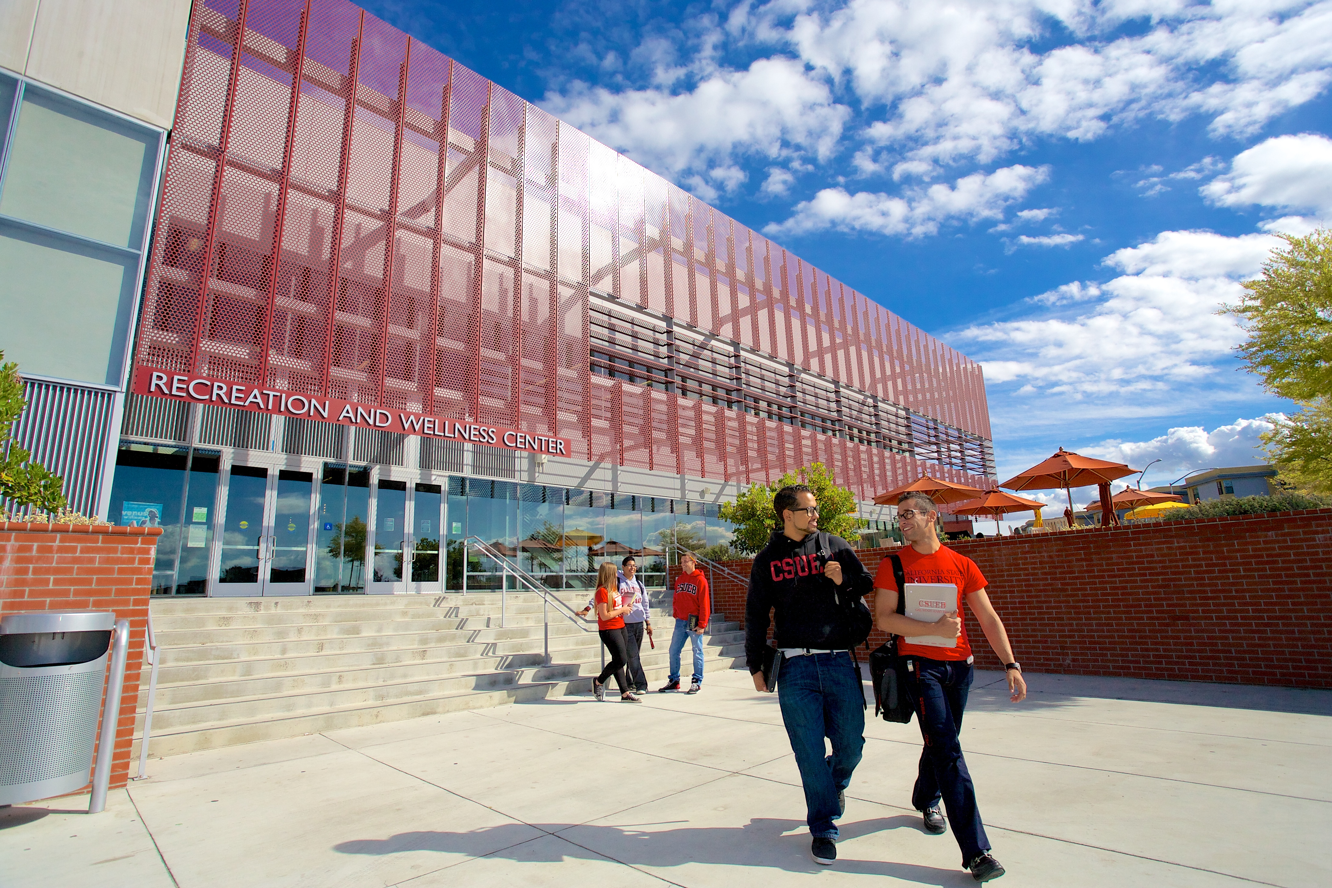 Students walking in front of a modern Recreation and Wellness Center featuring a striking architectural design and outdoor seating.