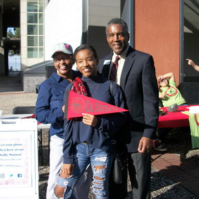 Three people Smiling while holding CSUEB flag