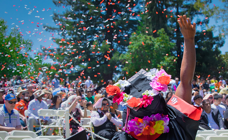 Graduate holding her hand up with confetti in the air