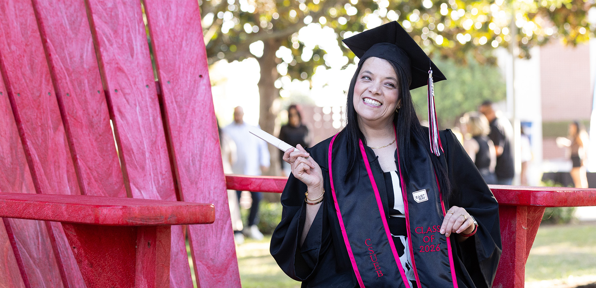 Graduate holding a diploma and posing by the big red chair