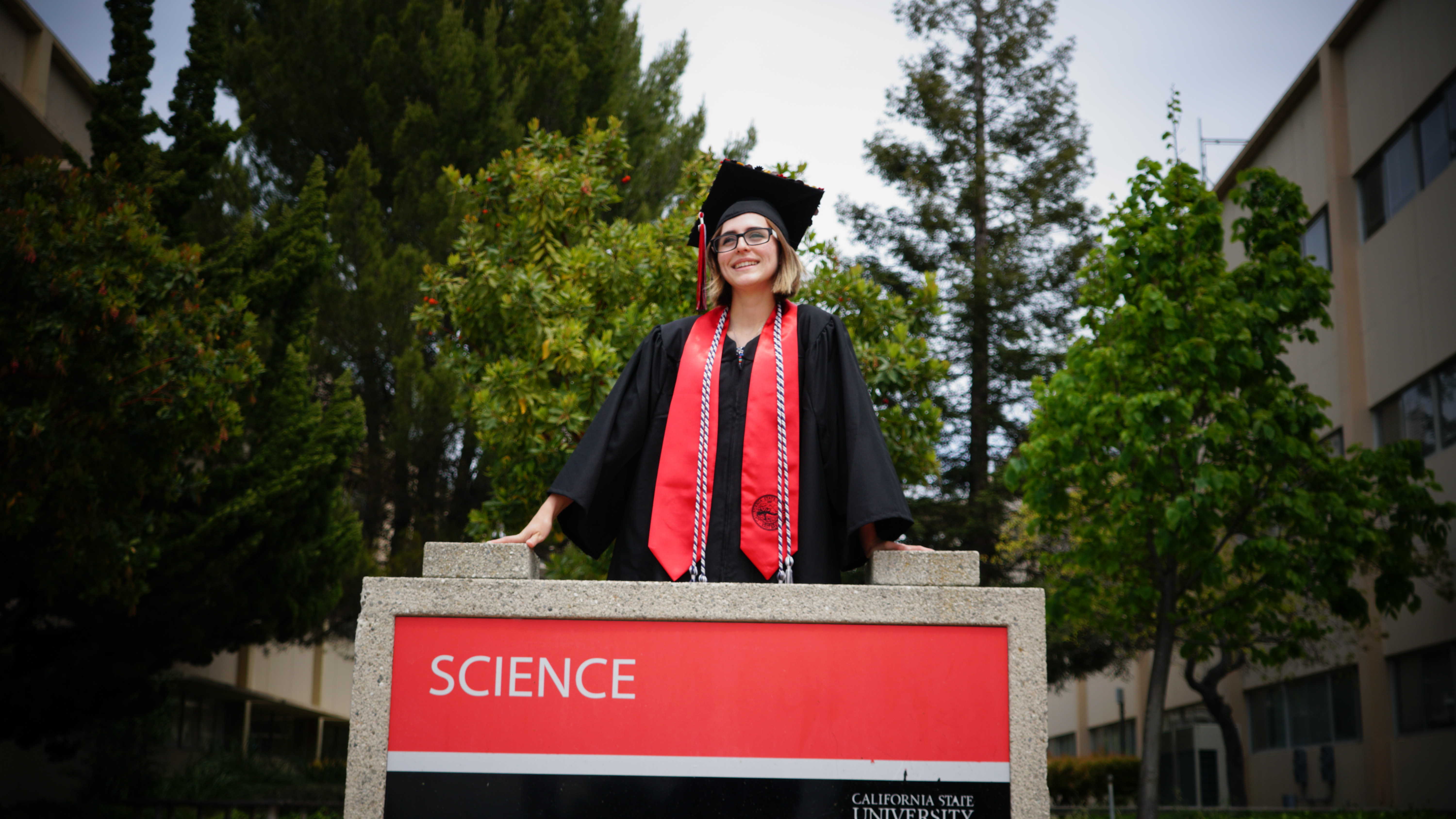 CSUEB student standing in front of Science buildings in cap and gown