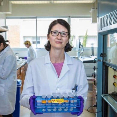 women in a lab looking at the camera while holding a rack of tubes