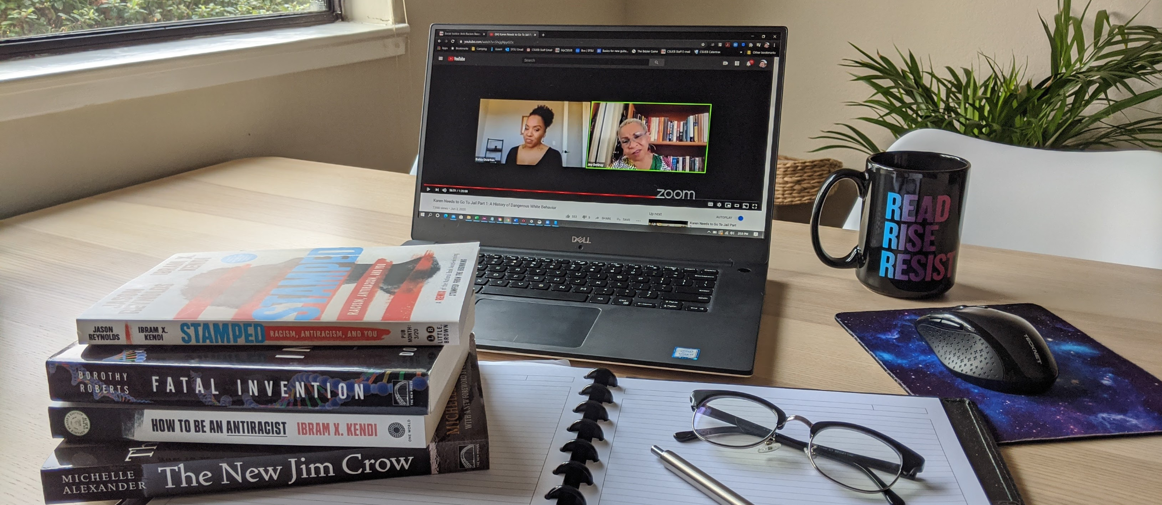 Desk covered with a stack of antiracist books and a laptop playing a webinar.