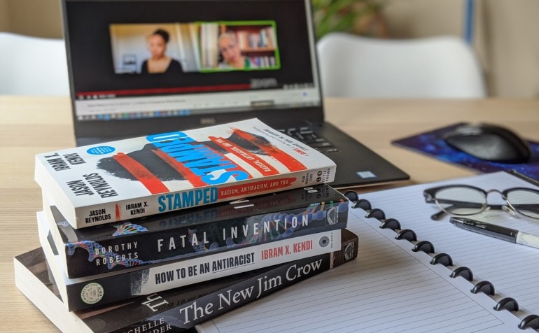 Anti-racist books stacked on a table infront of laptop.