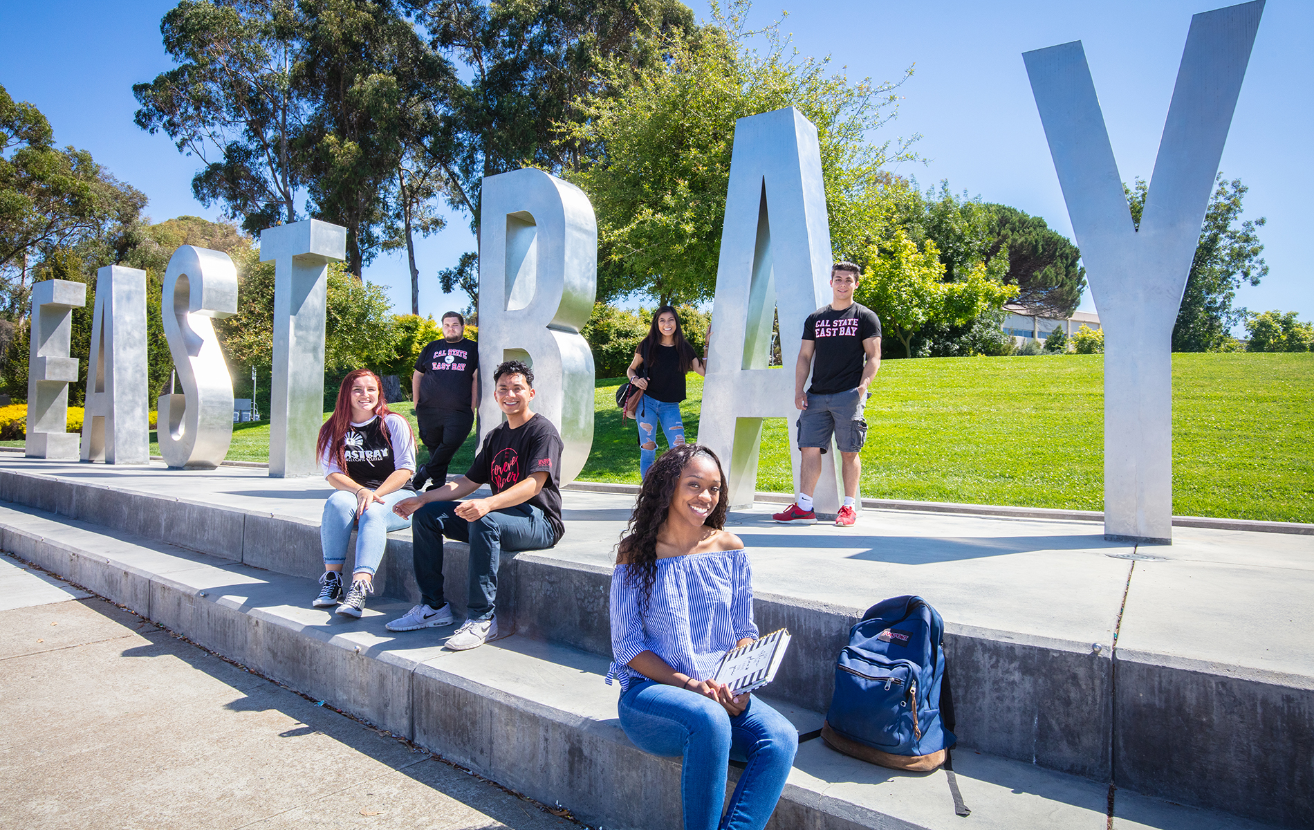 Cal State East Bay students sit in front of monument East Bay letters