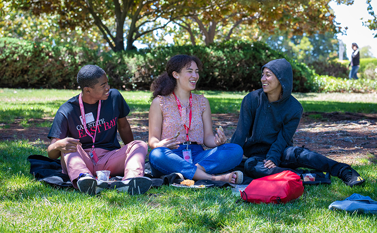 Three students sit on grass