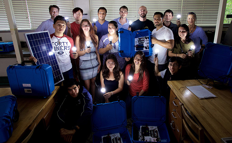 Group stands with solar suitcases lighting up dark room