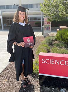 Woman in graduation attire holds program near Science building sign