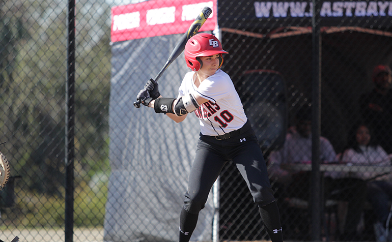 Female athlete in batting helmet and holding bat watches for the ball