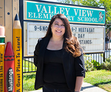 Woman stands next to elementary school sign