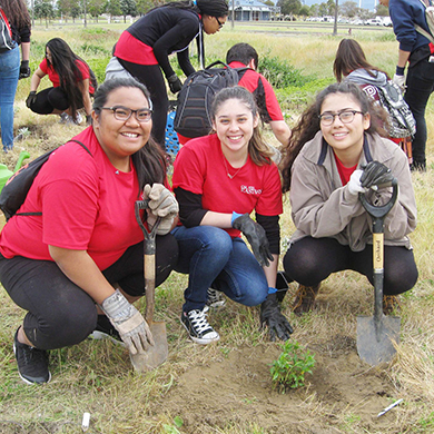  Three female students in red shirts crouch in a garden