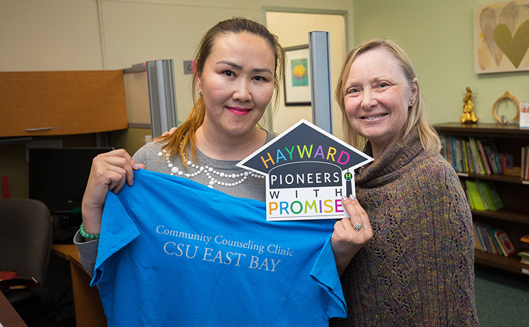 Two women pose with blue shirt and Hayward Promise Neighbhorhoods logo