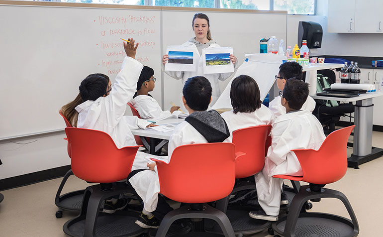 Student teacher in white coat teaches students at table