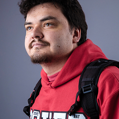  A male with dark hair, red sweatshirt and backpack on his shoulder looks into the distance