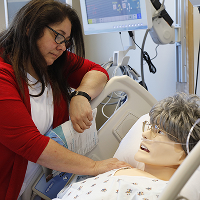  A woman in a red sweater puts her hand on the shoulder of a dummy laying in a hospital bed