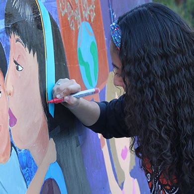  A woman paints a colorful mural featuring a female's face