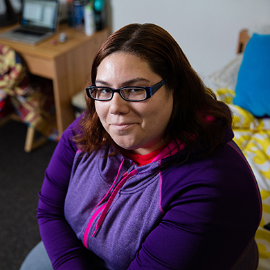  A young woman in glasses and a purple sweatshirt poses