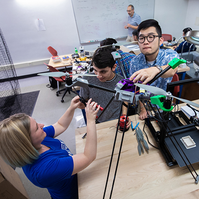 Three students add wiring to to an object with legs and propellers. 