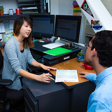  A woman at a desk looks over a piece of paper with a male student