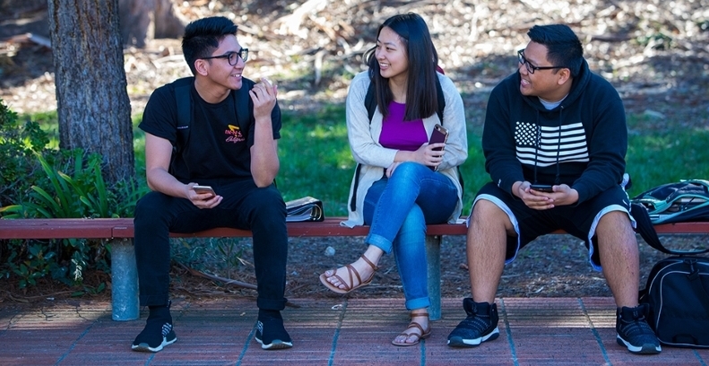 Three students sitting together on a bench on campus