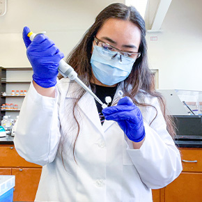 student standing in lab coat experimenting 