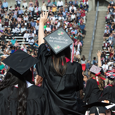 Graduate raises her hand with crowd in background