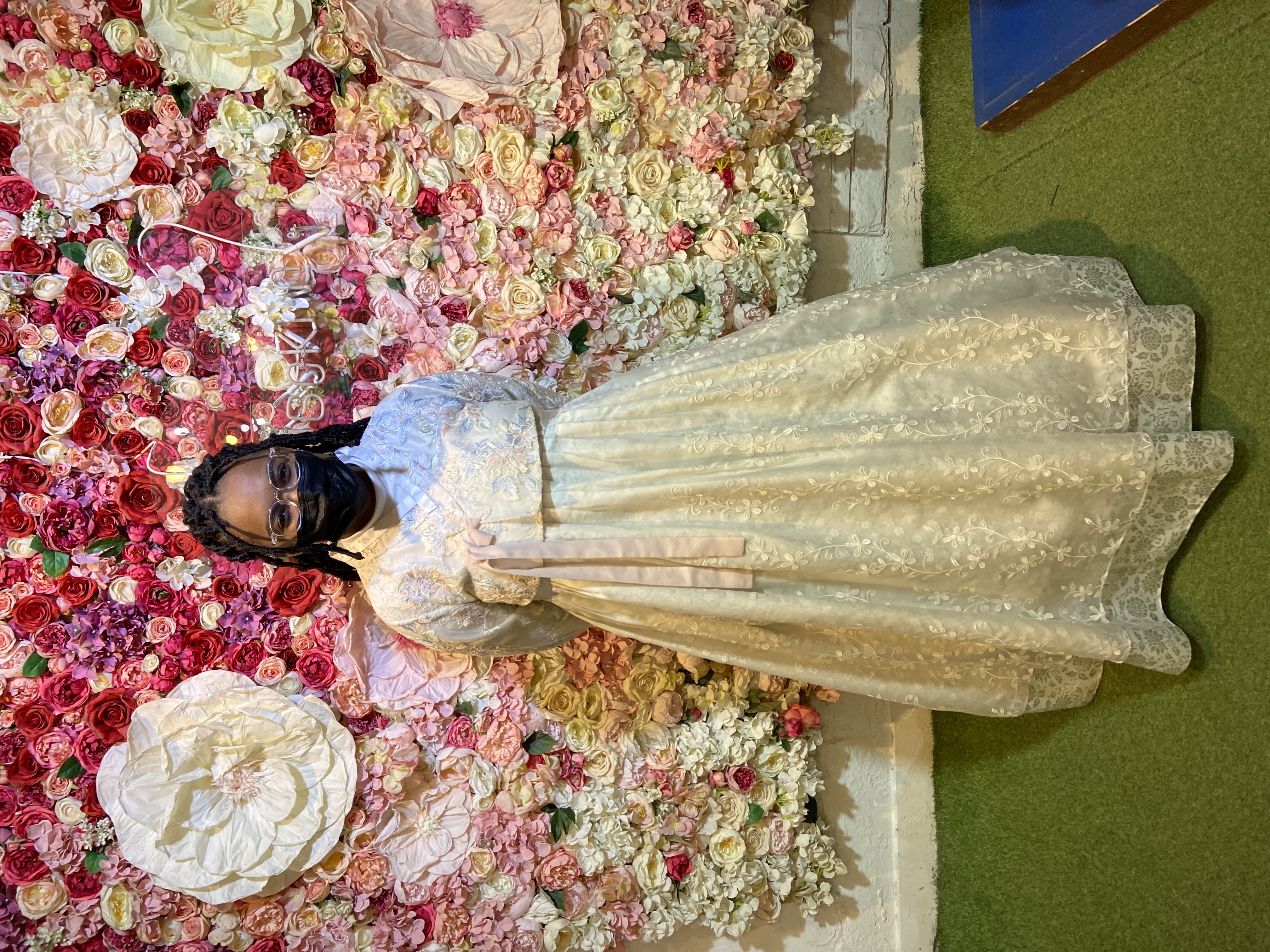 woman with mask smiling in front of paper flowers