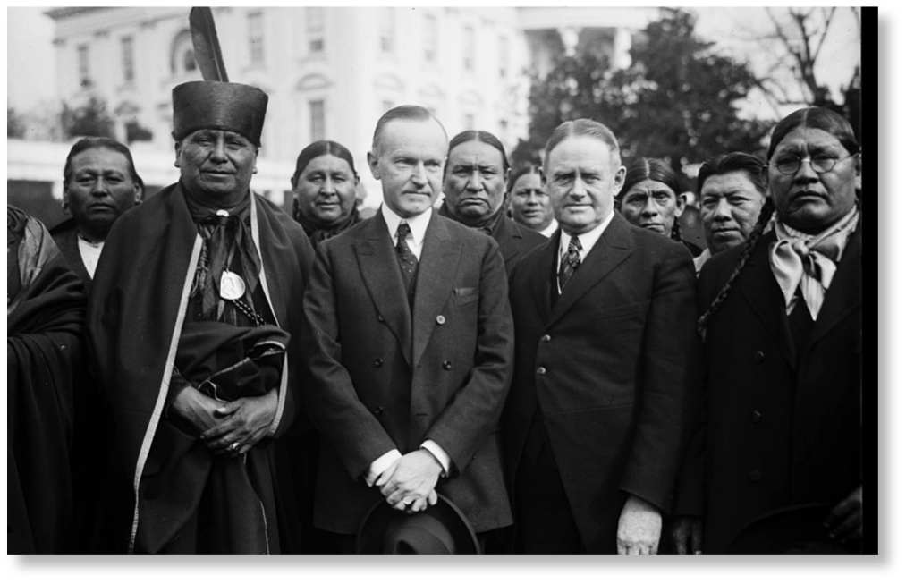 black and white photograph with 2 white male standing with a group of indians