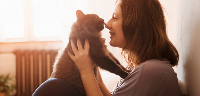 Woman smiling and holding her pet cat as it licks her nose