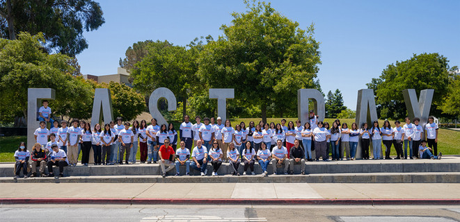 Engineering camp students wearing Chevron T-shirts in front of the East Bay letters