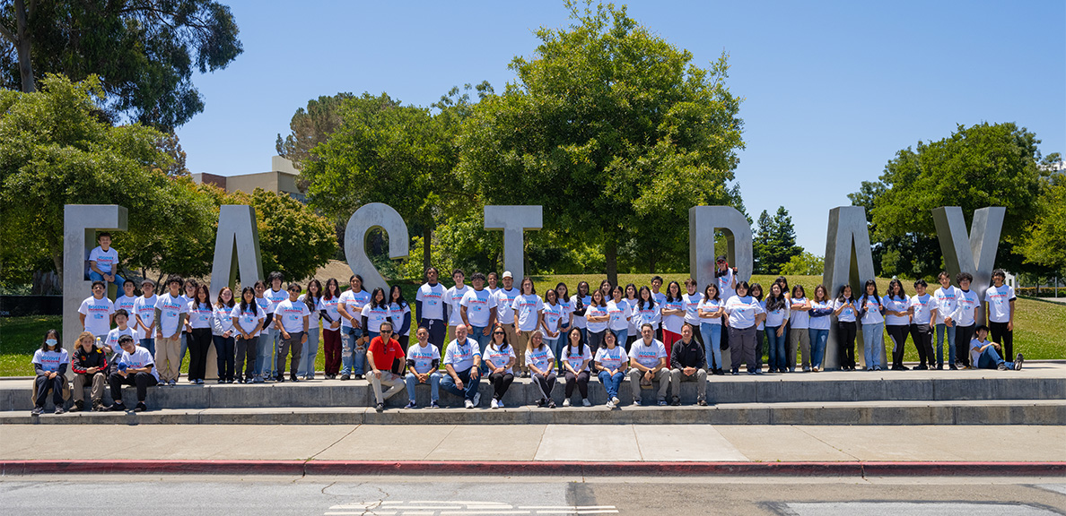 Engineering camp students wearing Chevron T-shirts in front of the East Bay letters