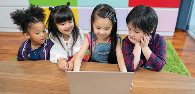 Four children of diverse backgrounds sit together looking at laptop screen