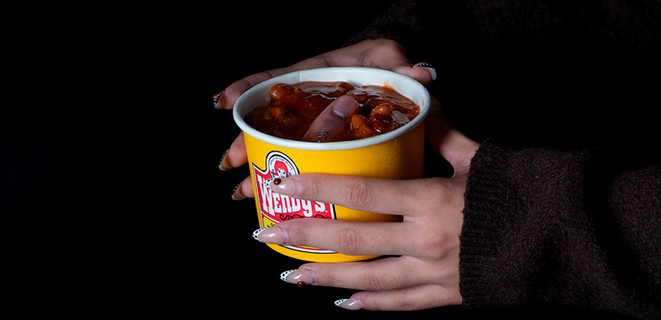 Two hands holding a bowl of Wendy's chili, with a thumb sticking out from the middle. The background is dark, giving it a mysterious feeling. 